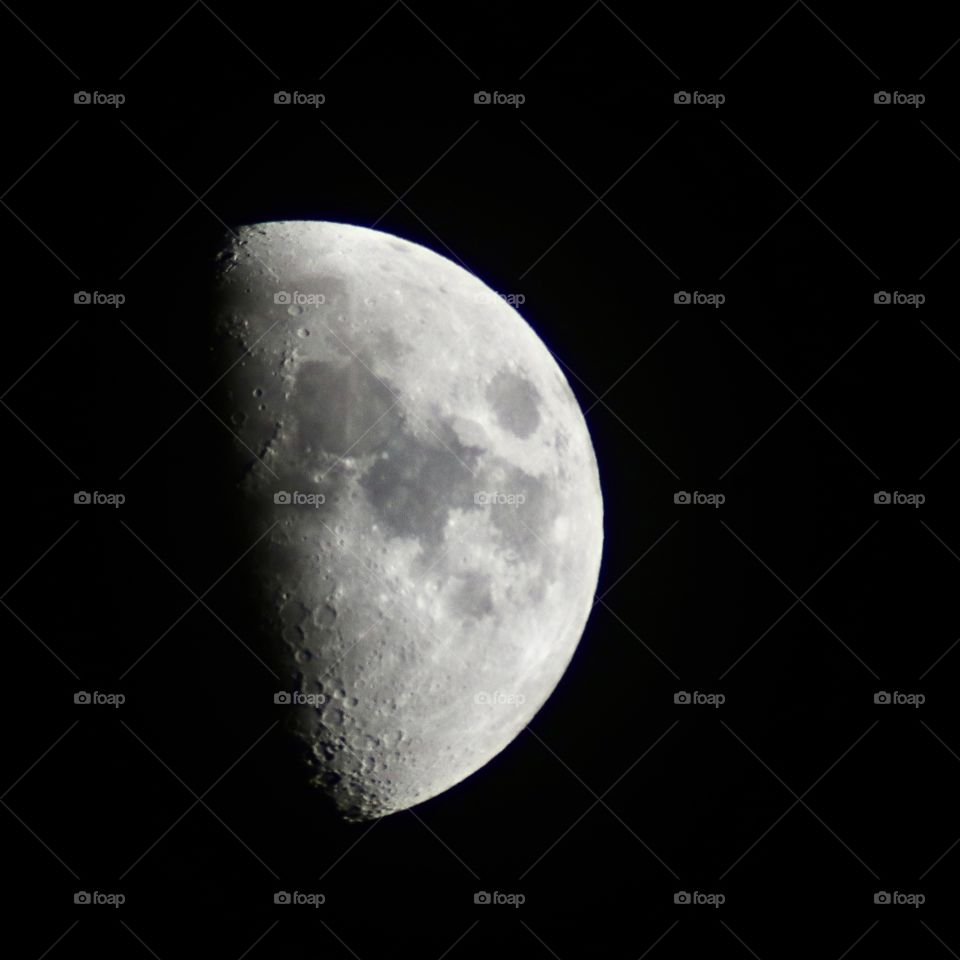 Moon shines on a dark night sky, half of it illuminated with the sun’s light.