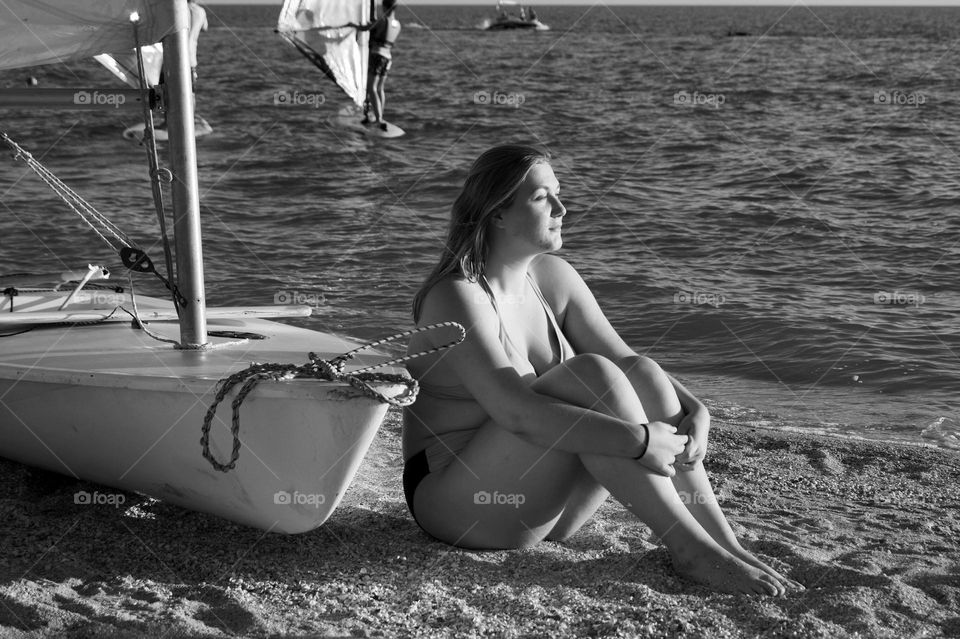 a young girl sitting on the beach near the boat⛵