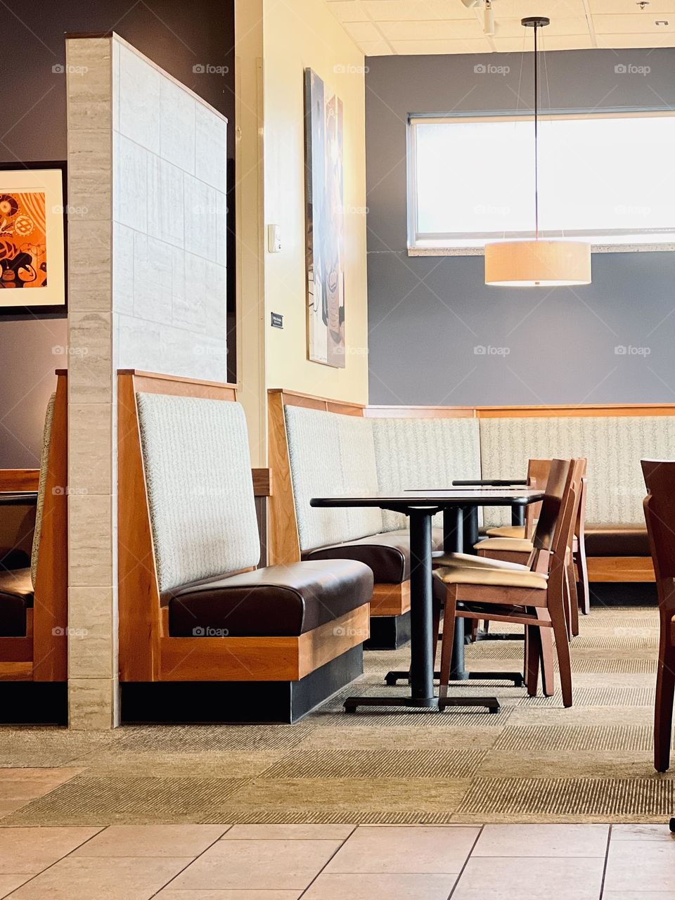 Simple lines and wooden furniture of cafe interior. Drop lighting and bright natural light from high window, carpet and padded benches.