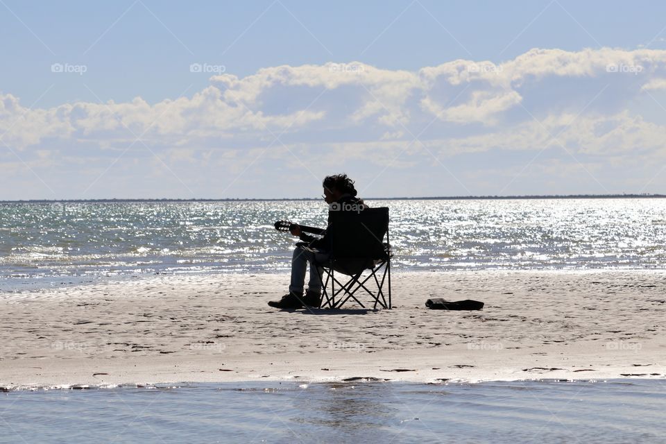 Lone guitarist sitting in chair on beach partial silhouette 