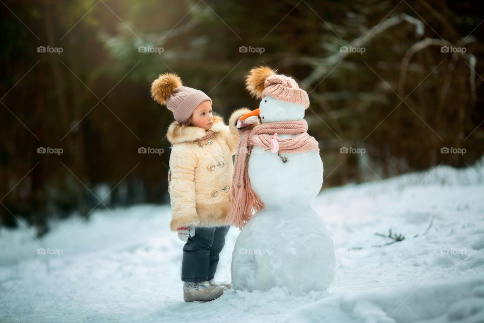 Little girl with snowman in winter park