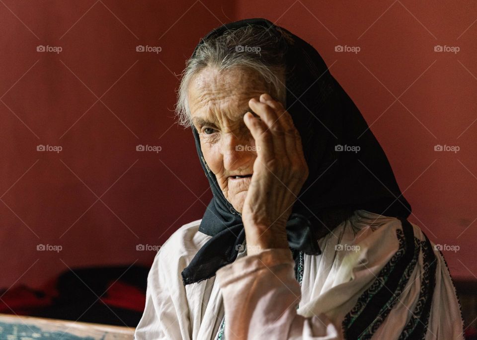 Old woman dressed in a traditional romanian blouse being sad, because she lives a very hard life in a remote countryside village.