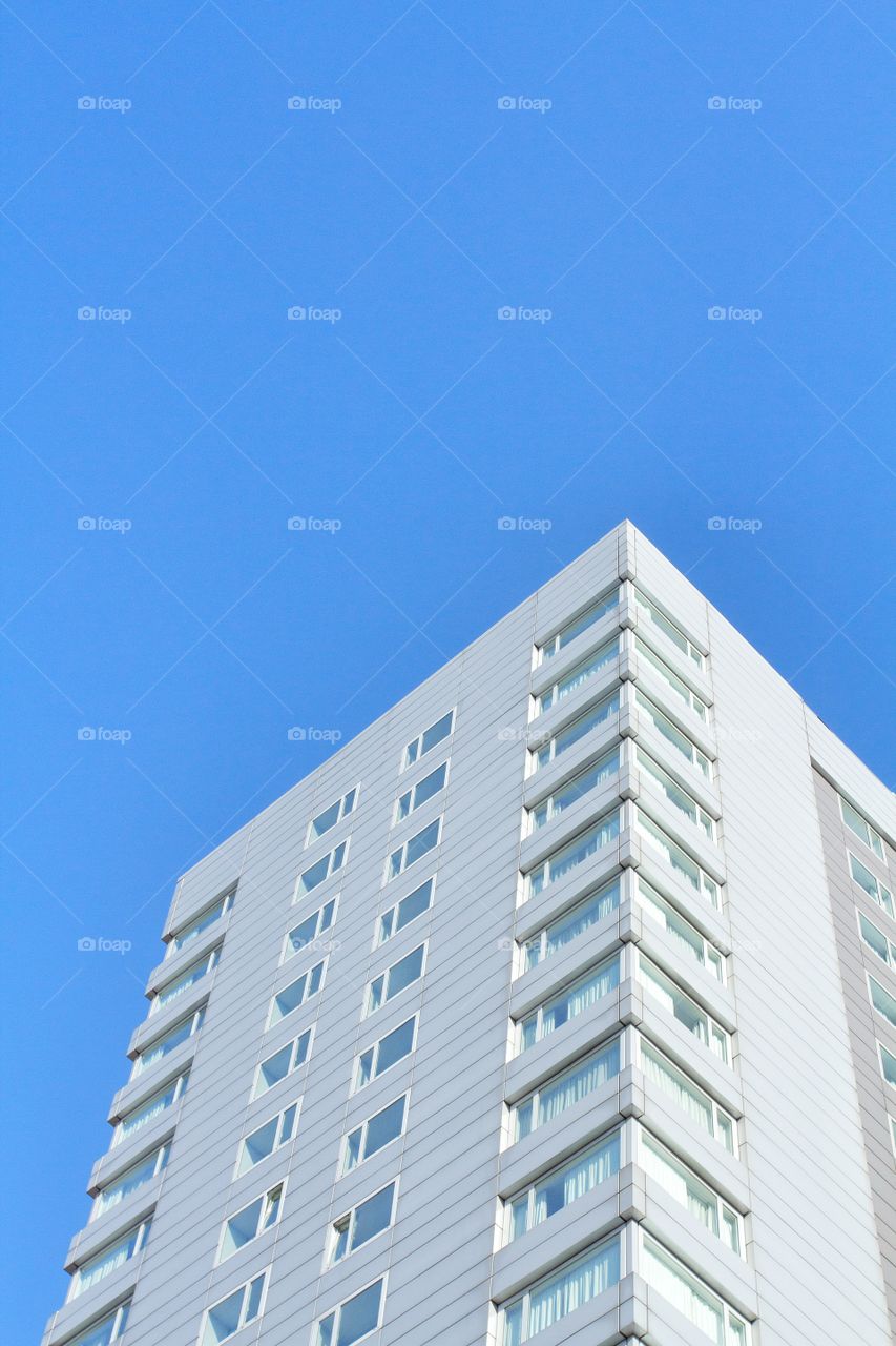 Looking upwards to a tall, white, residential skyscraper under a bright blue sky. 