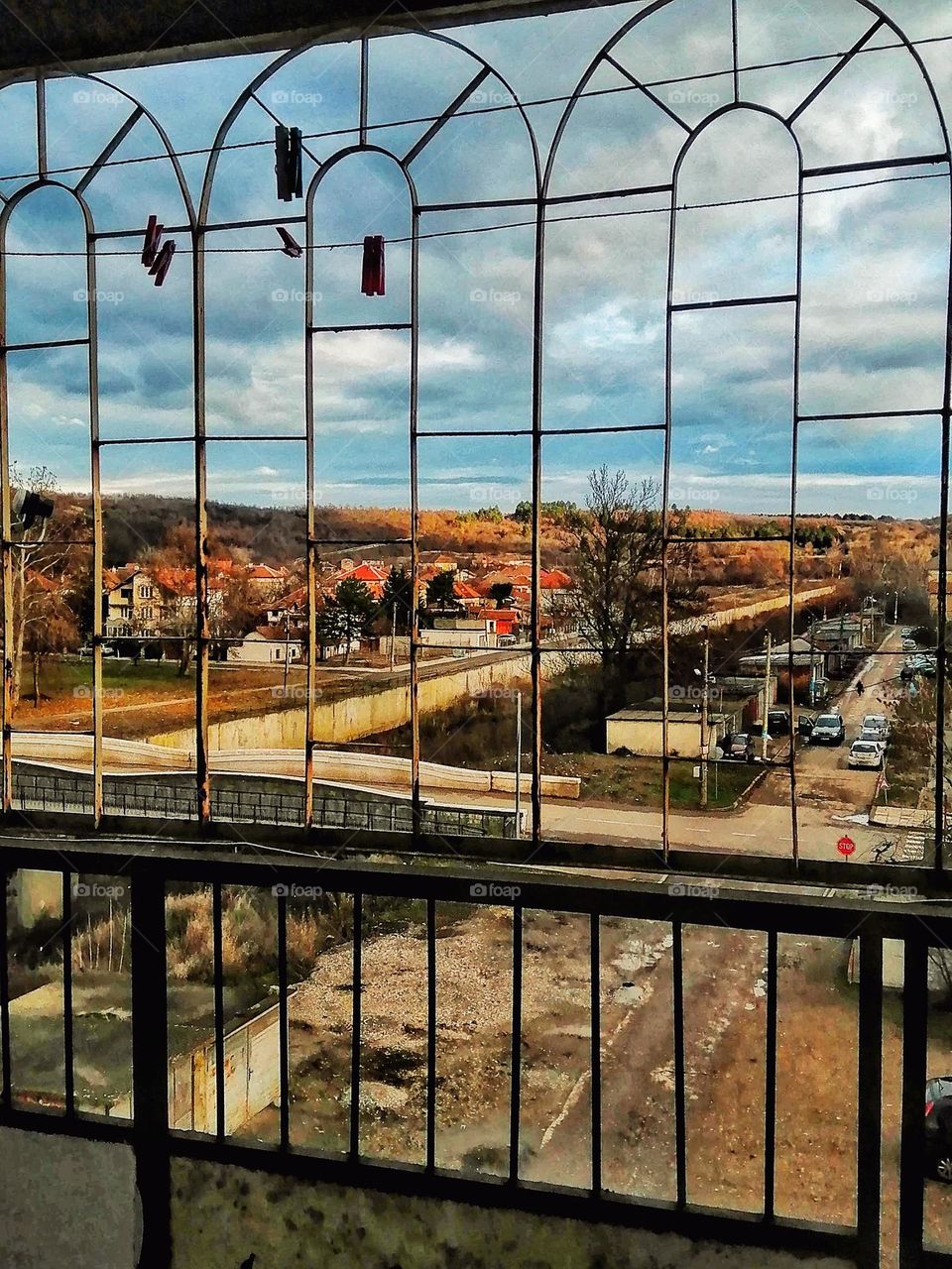 A photo behind the bars of a balcony in a town in Bulgaria with its beautiful view of houses and roads and hills full of colours