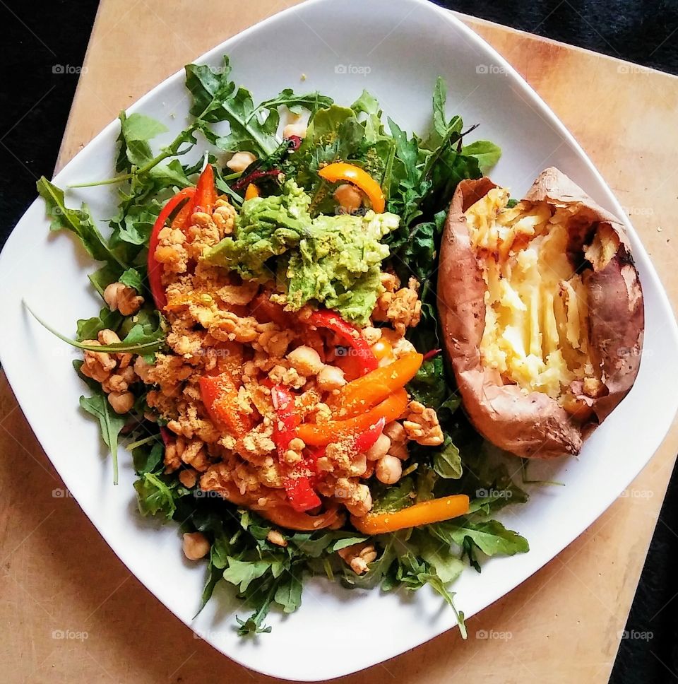 Sweet potato served with tempeh, chickpeas, peppers and avocado, all on a bed of arugula