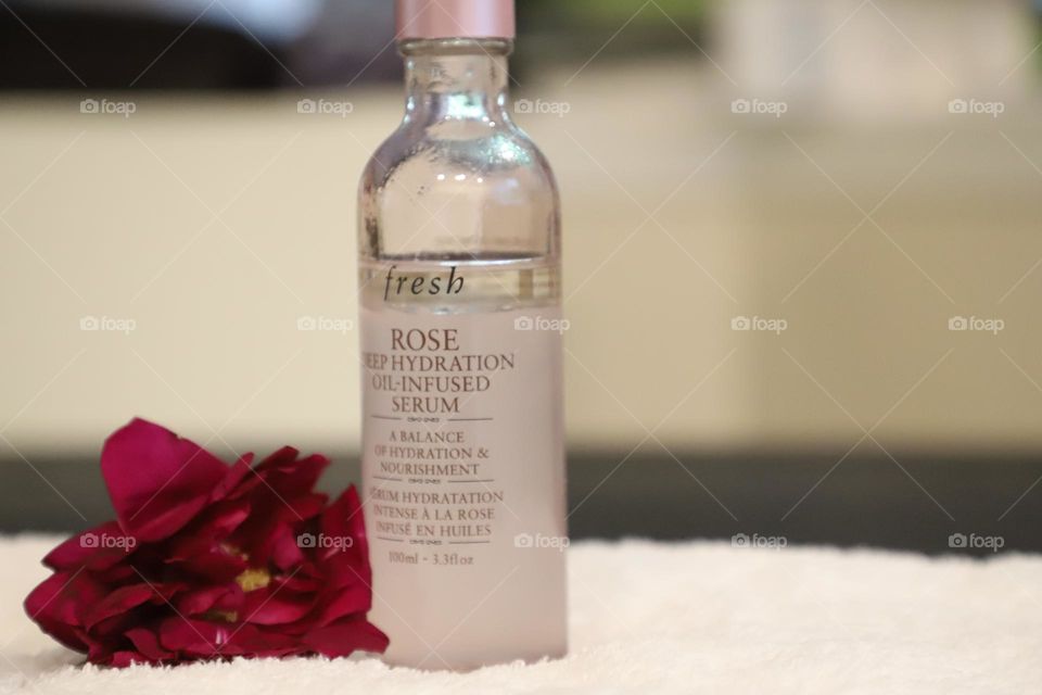 Facial oil on a white towel , red flower behind it