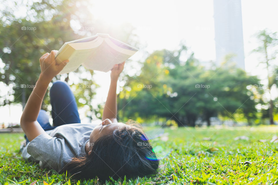 Asian teens girls are lying reading a book on the grass in the park