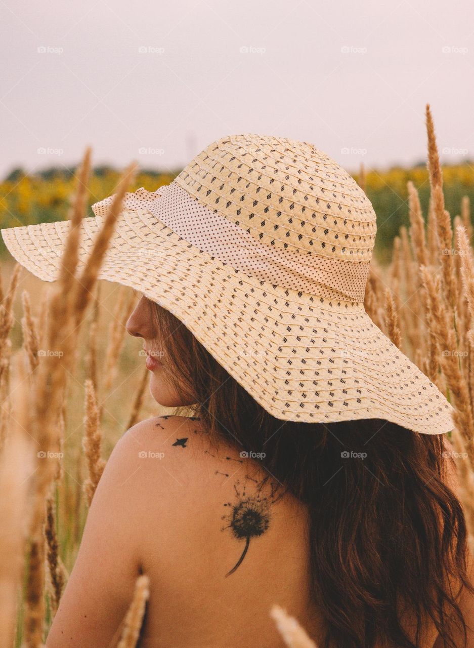 Young woman with a dandylion tattoo on her shoulder, wearing a hat on a hot summer day.
