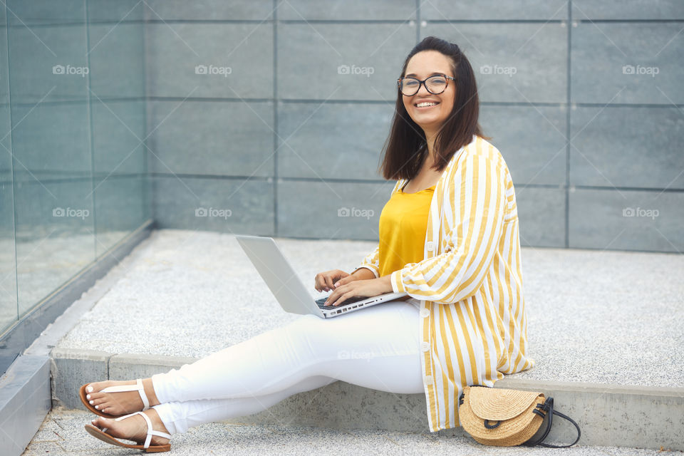 Portrait of smiling plus size woman 30-35 years old in fashion casual clothes, working with laptop outdoors in city park