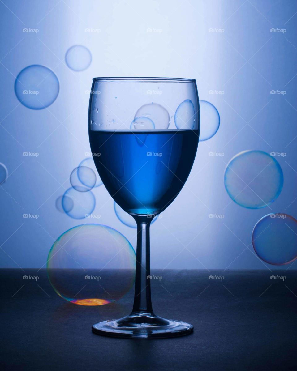 shades of blue image of a wine glass with bright blue liqueur in the foreground with blue accented bubbles floating scattered against a gradient blue background
