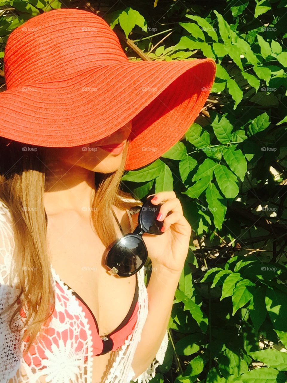 Selfie of woman with long dark blonde hair with black sunglasses in her hand standing against background made of leaves