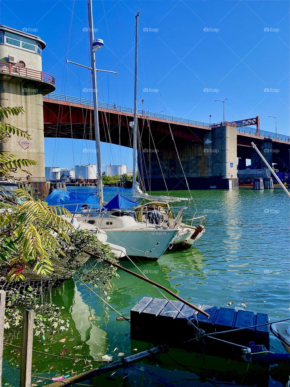 This is the “Pulaski Bridge” at “Newtown Creek” in LIC, Queens seen from the narrow strip of land on the LIC shore. To add an idyllic vibe two sailboats that are moored here can also be seen. 2023. Hypnotic Productions
