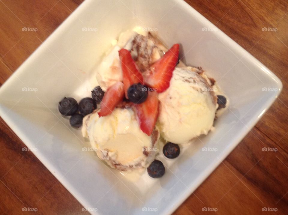 A photo of Vanilla ice cream with strawberries and blueberries. 