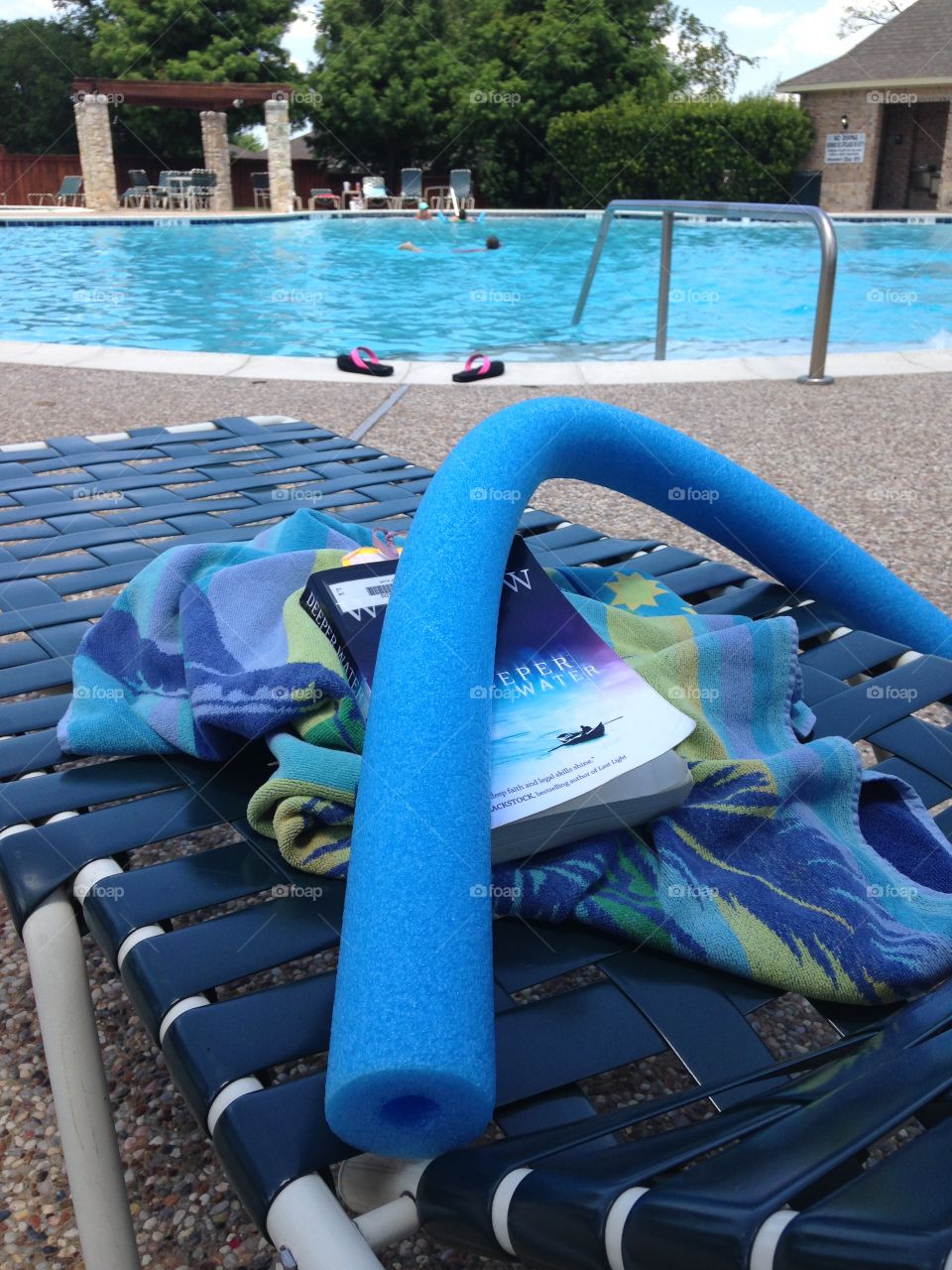 Summer relaxation. Towel, pool noodle, and book on a lounge chair by the pool