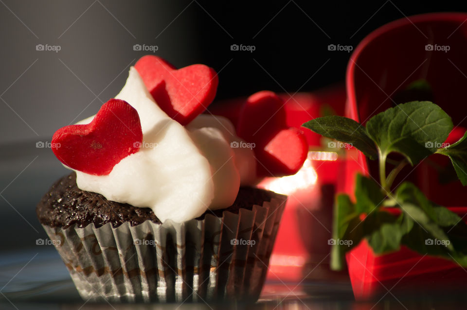 Dessert love three red hearts decoration on a beautiful  chocolate cupcake with rich buttercream frosting  on table with fresh mint leaves on vine and red cookie heart cutter 