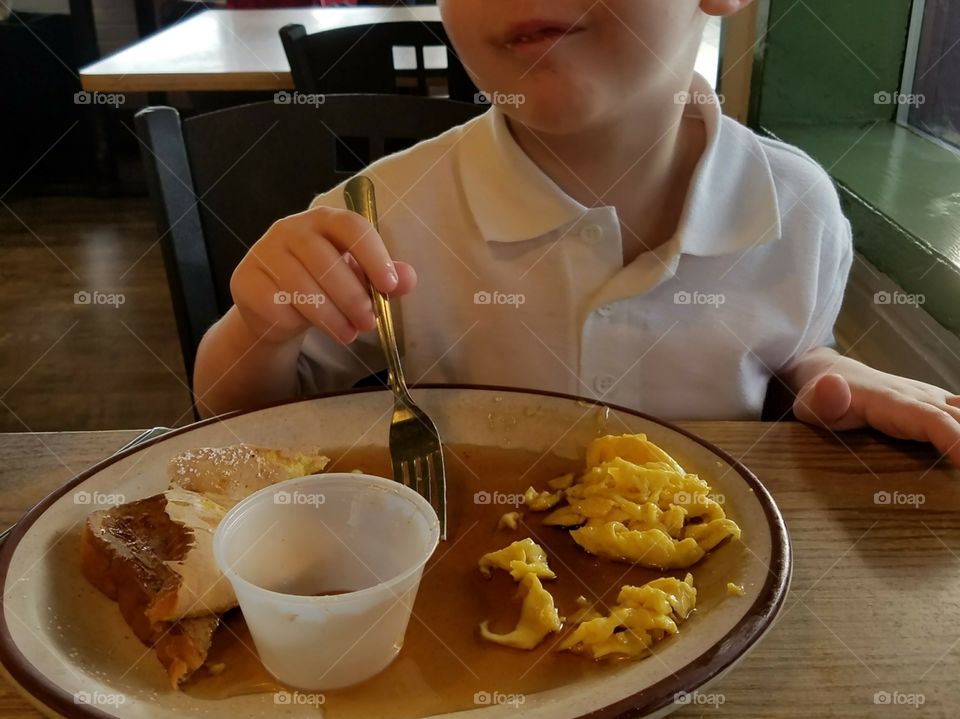 Young boy exhibits a look of content as his french toast and scrambled eggs swim in a bed of sticky syrup.
