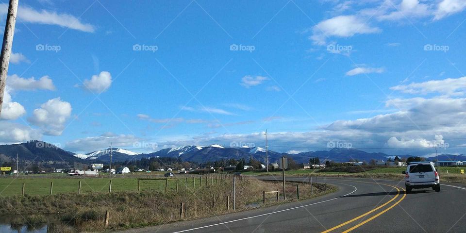 A country road, blue sky, and distant, white-capped mountains