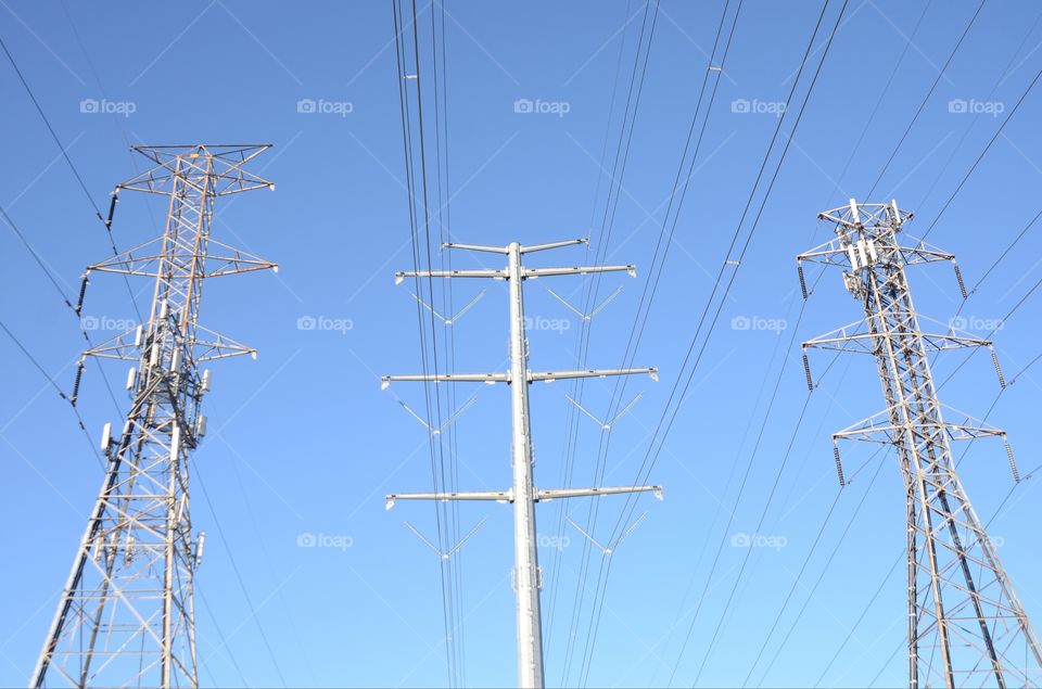 Three high tension electric towers stand tall side by side.