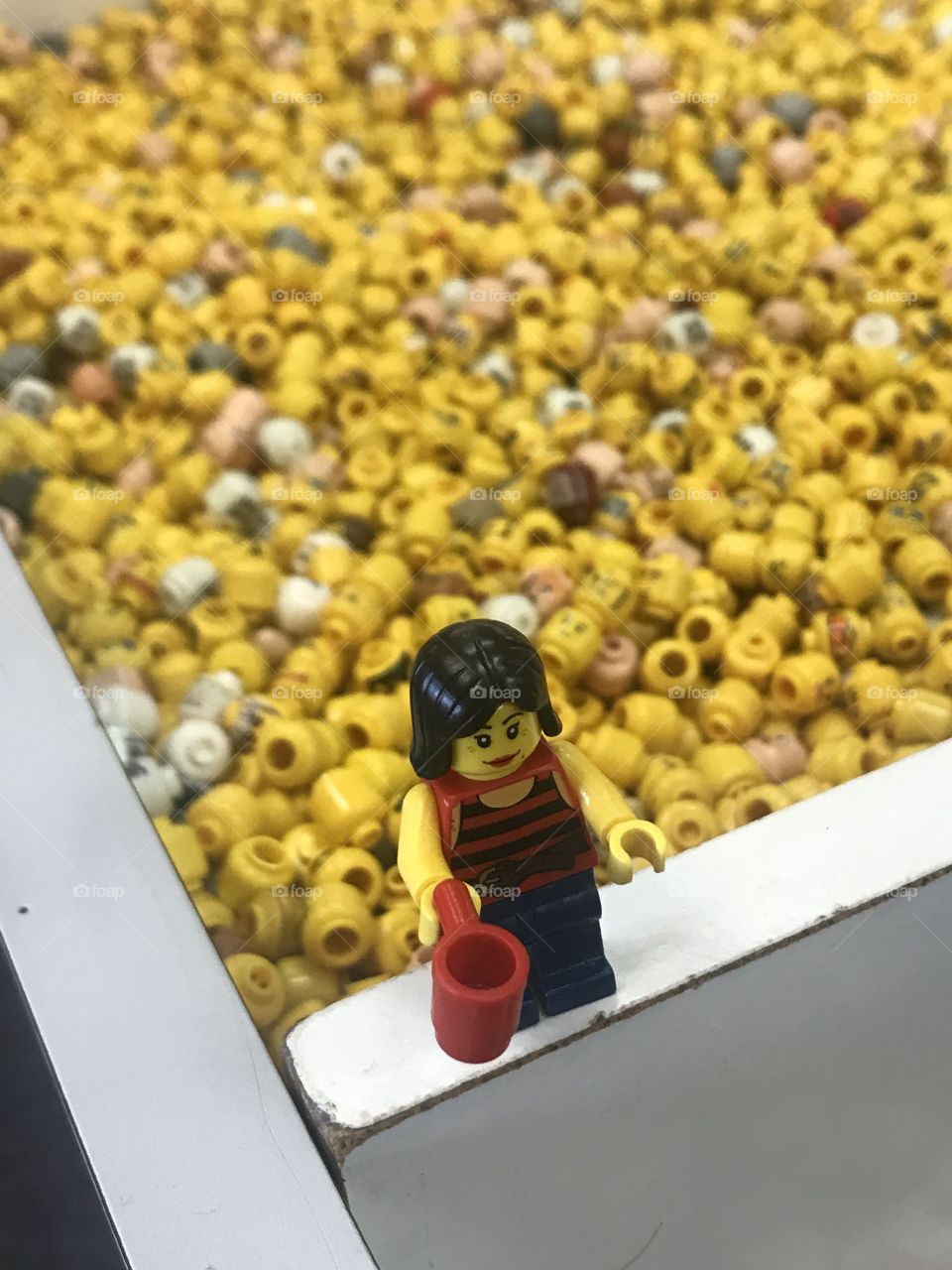 LEGO woman with coffee cup pictured in front of bin of LEGO figure heads. 