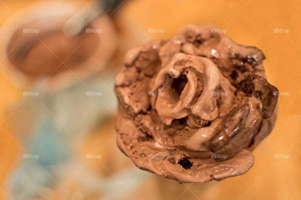 Chocolate ice cream cone rose with heart shape center on wood table with tub of ice cream and scoop in background decorated with brownie pieces for National Chocolate Ice Cream Day with copy space