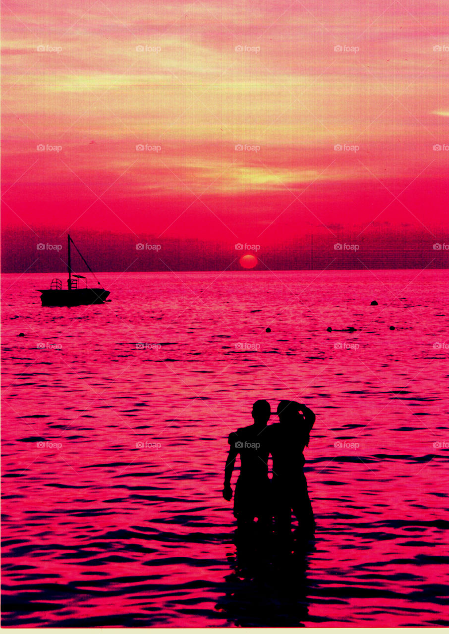 Negril Beach Romantic Sunset. Couple in water at Negril beach Jamaica watching a romantic red pink and yellow hued sunset