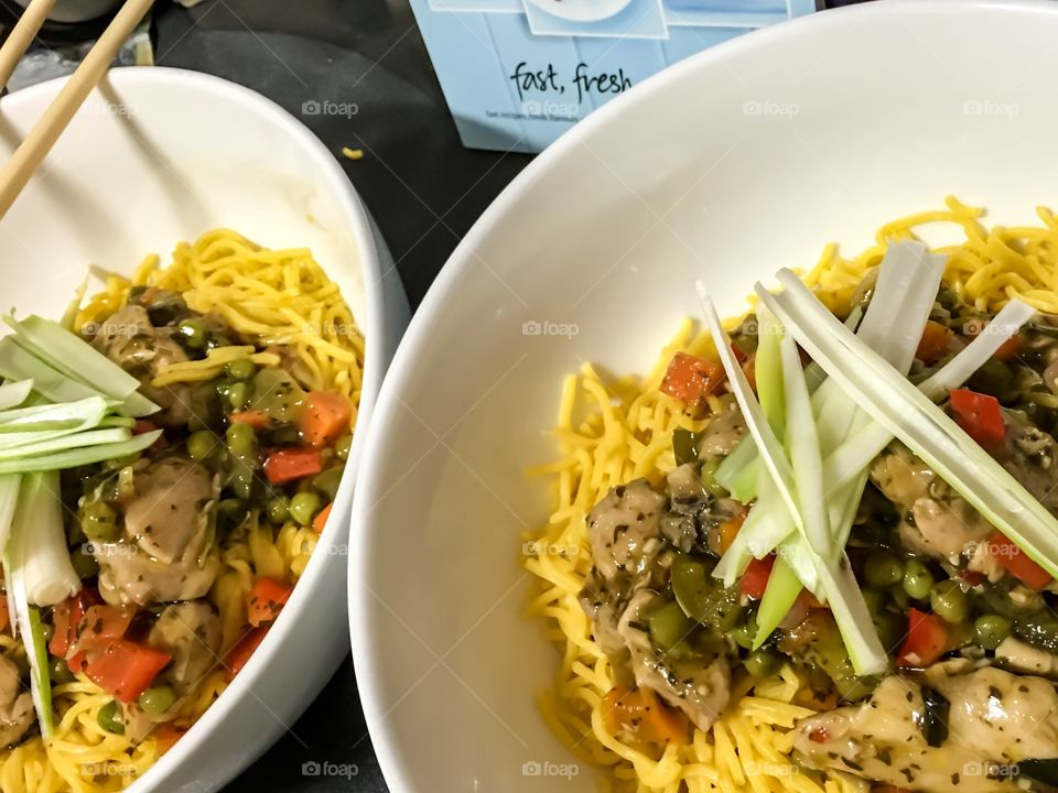 Basil chilli Thai chicken and veggies on Singapore noodles in white bowl with chopsticks Asian food