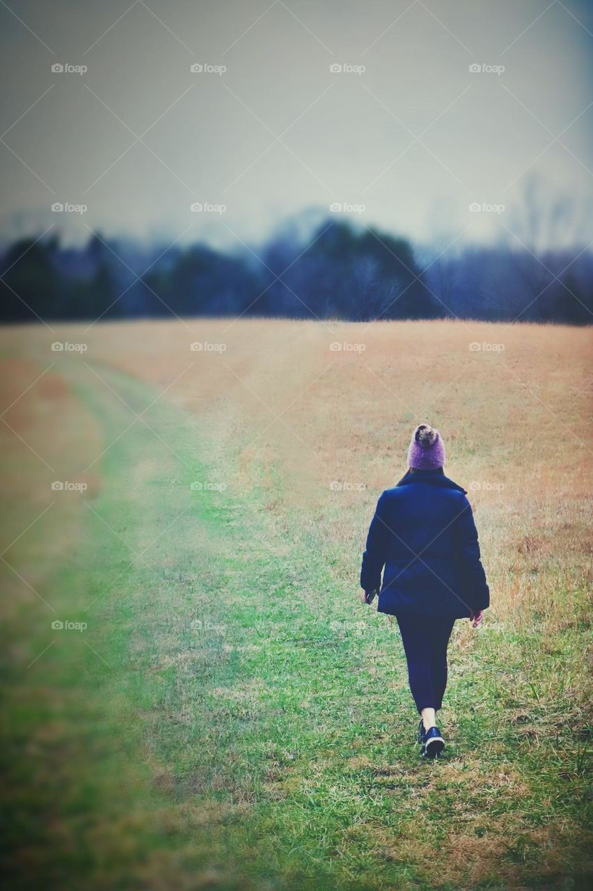 An athletically dressed female walks in a quiet meadow on an overcast day in the Winter