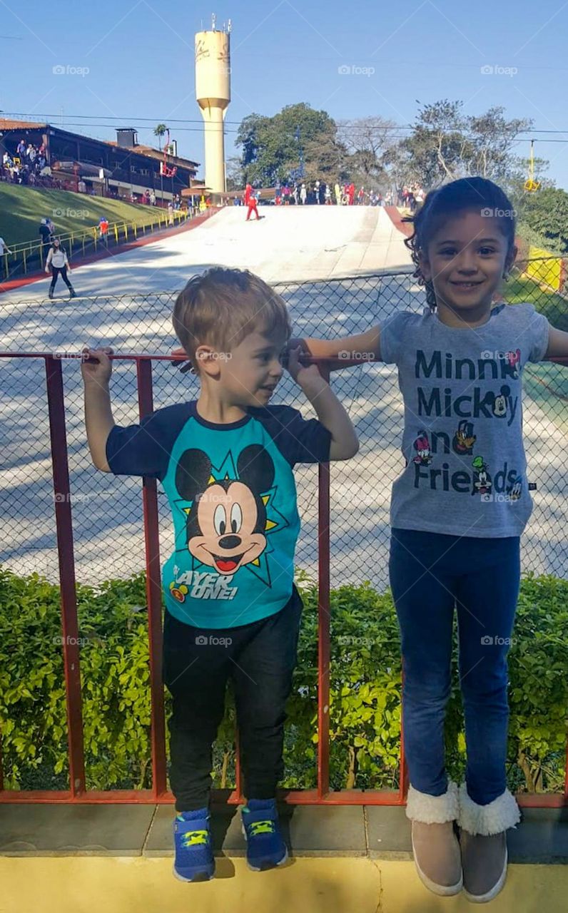 As it doesn't snow in Brazil, we don't have ice or snow for winter sports. The solution was to build an artificial ski slope. In the photo, two children in front and in the back, artificial ski slope, cable car and skiers practicing the sport.