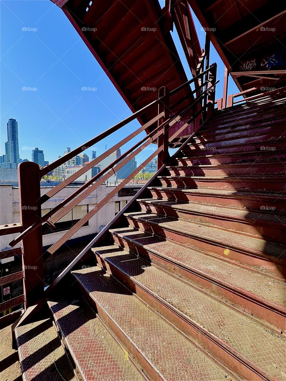 This is the red metal staircase of the “Pulaski Bridge” at “Newtown Creek” in LIC, Queens. The late afternoon sun casts deep shadows that are distorted according to the shape of the steps which creates interesting patterns. 2024. Hypnotic Productions