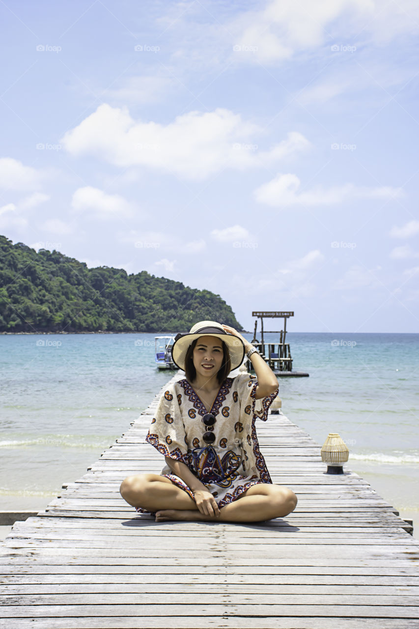 Women Wear a hat on the wooden bridge pier boat in the sea and the bright sky at Koh Kood, Trat in Thailand.