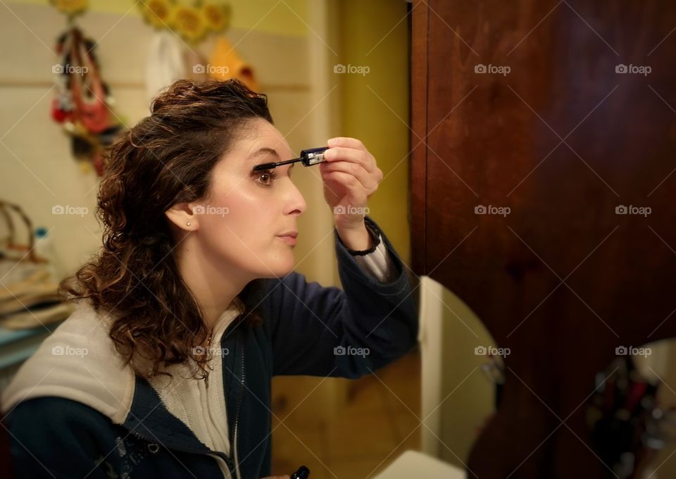 Woman puts mascara in front of the mirror