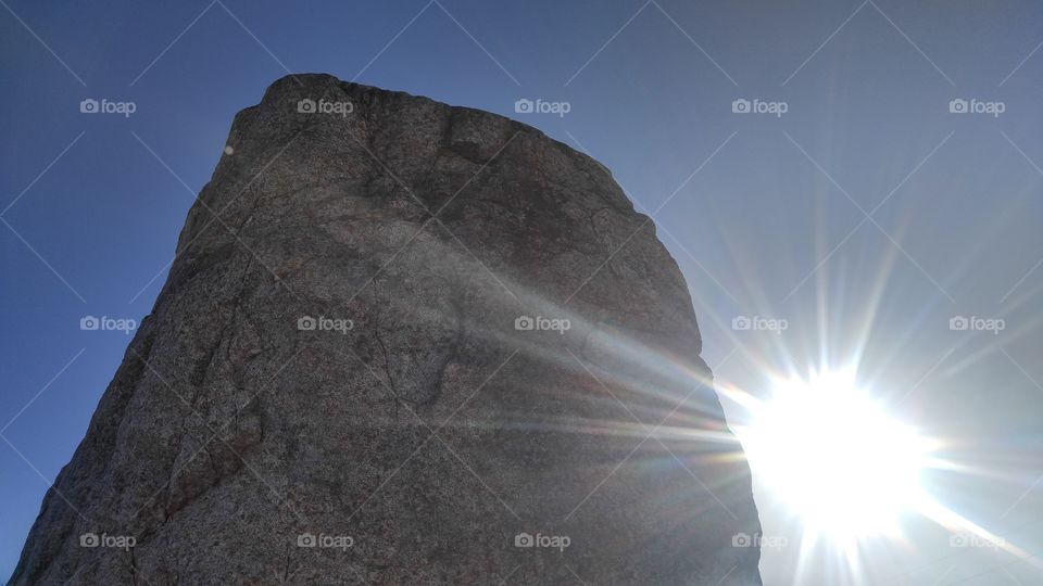 sun peeking out from behind a huge rock
