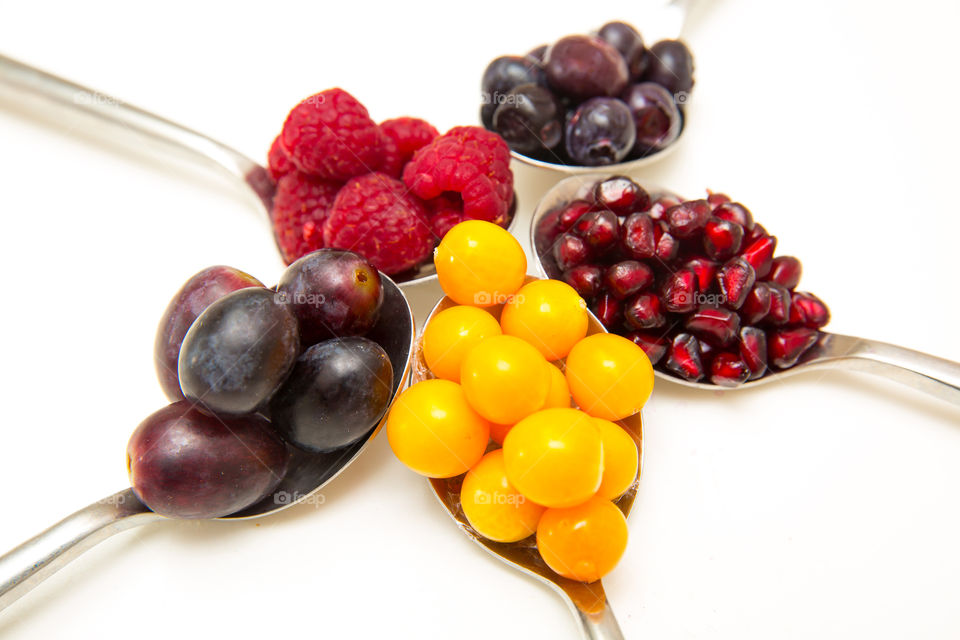 I love fresh fruit and add different varieties to my diet. Close up image of various fresh summer berries en fruits arranged on spoons and a white background.