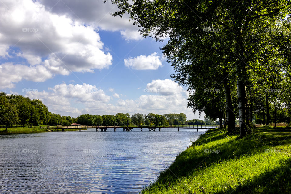 A portrait of the lake at bussloo in the netherlands on a sunny day with a blue sky with some cloads. on the lake their is a bridge to cross it quicker.