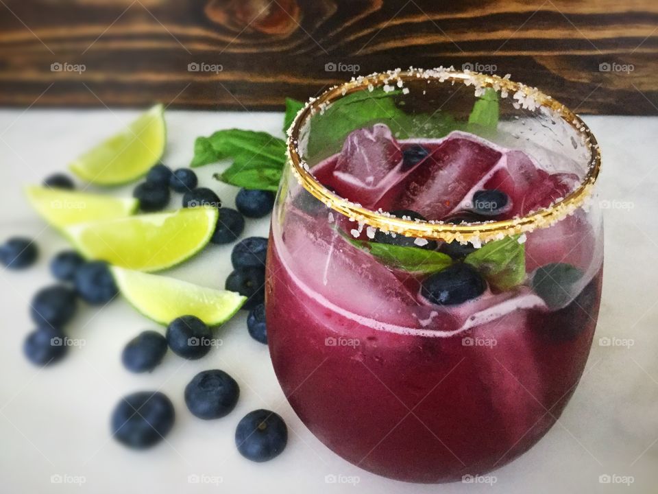 Blueberry mint mojito with salt rime, shown with blueberries and limes, and garnished with mint leaves