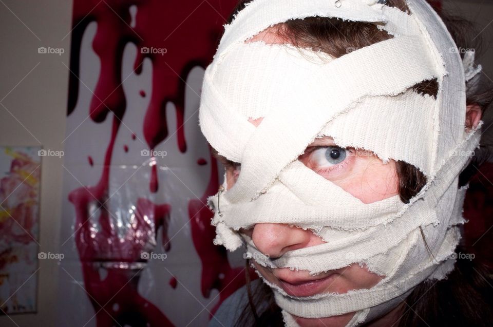 A young woman in Halloween mask of bandages looks at the camera.