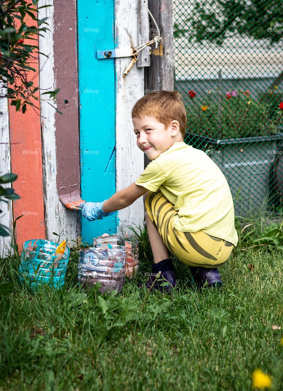 Child red-haired boy paints the fence