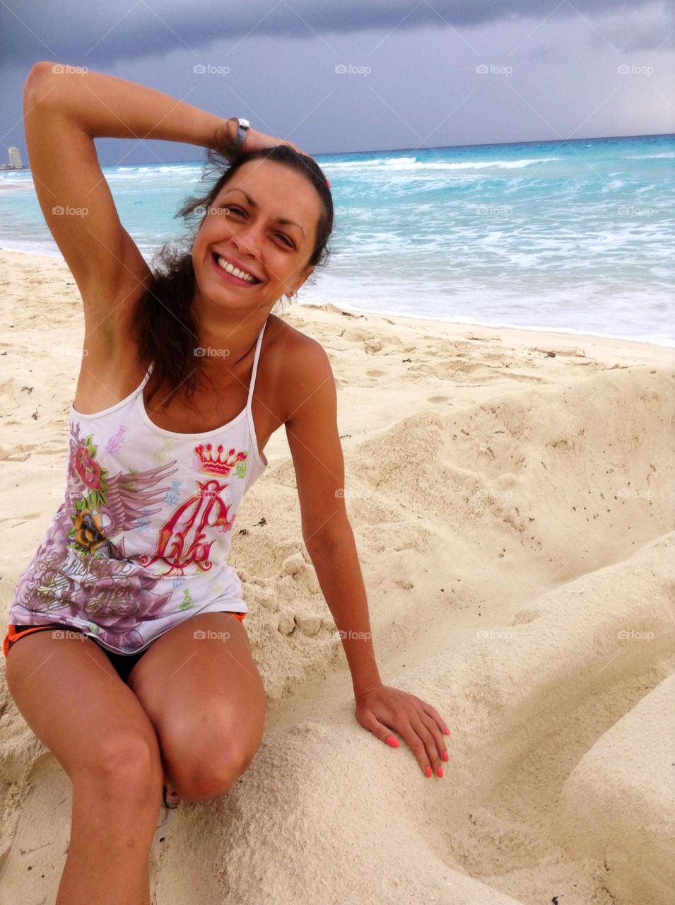 girl in a T-shirt and shorts sits on the beach at the sea and laughs.