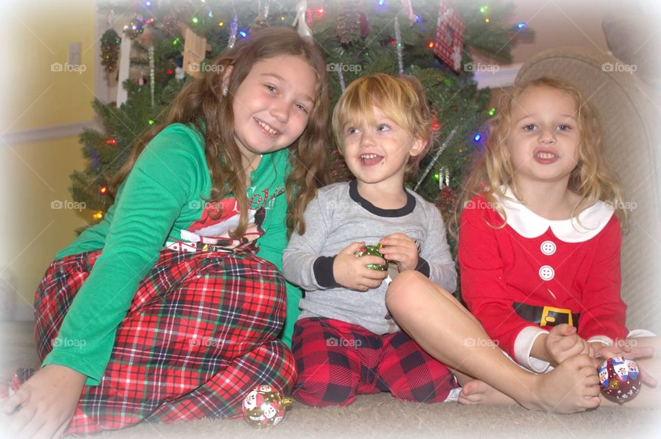 Three adorable siblings in front of their Christmas tree. 