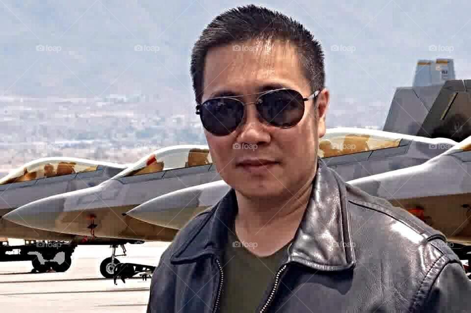 A man wearing a jacket and glasses is posing in front of some fighter planes in Indonesia