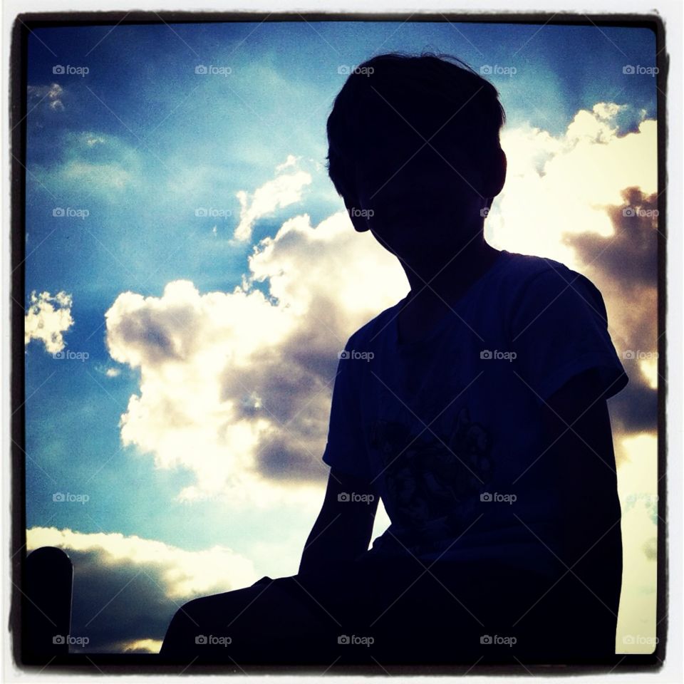 Silhouette of a boy . The boy is backlit by powerful clouds. Great photo. 