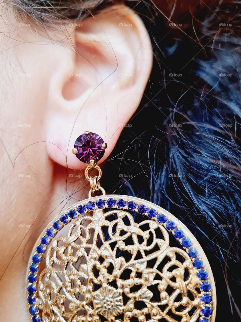 detail of gold earring with purple rhinestones worn by a woman with curly hair