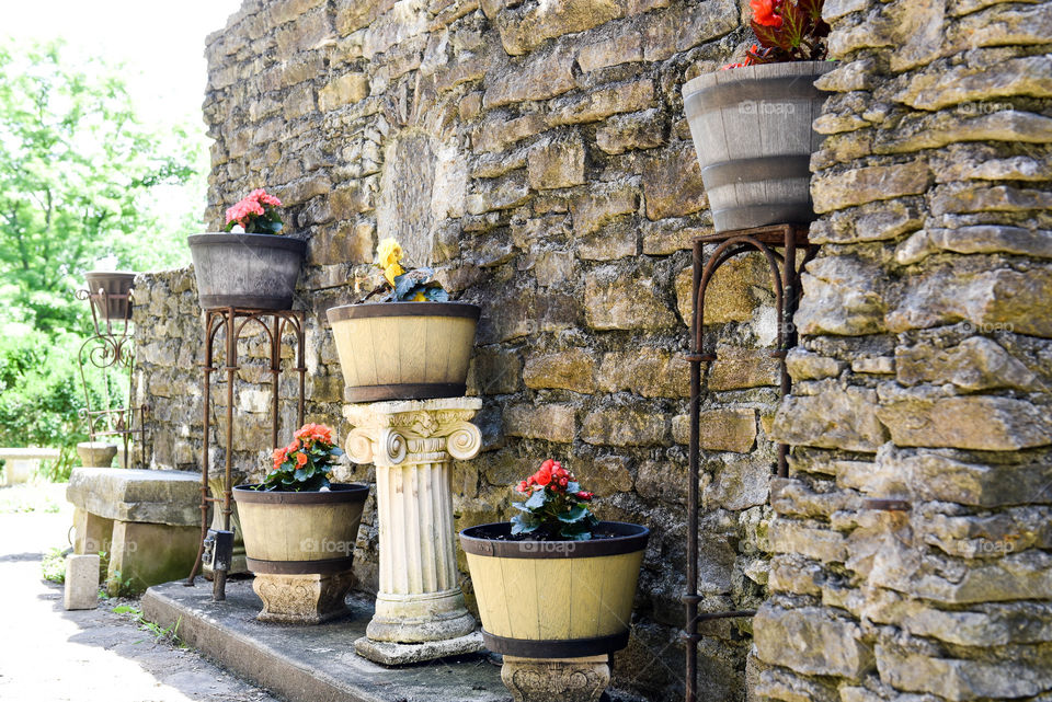 Row of assorted planters and stands against an old rustic stone wall outdoors