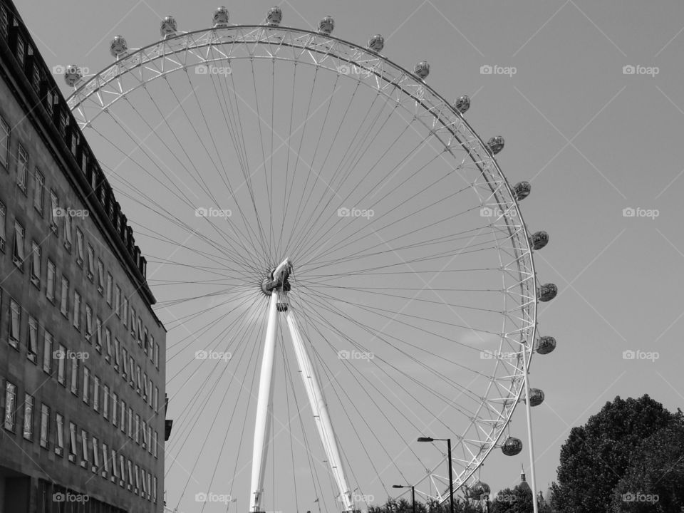 The London Eye towers above local historic buildings in London on a sunny summer day. 