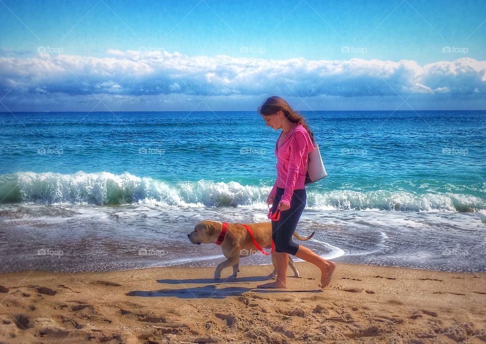 Young lady and her dog walking on the beach