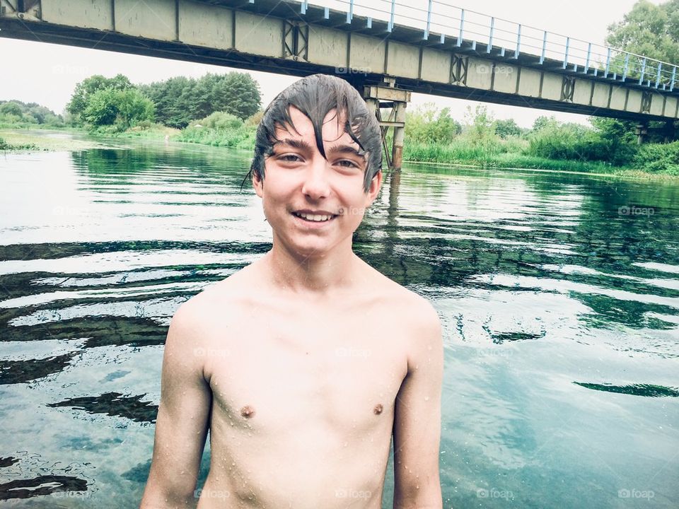 Young smiling boy standing in a river on summer day