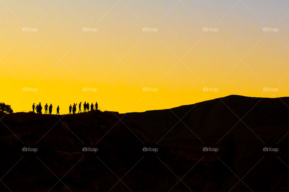 Bunch of friends looking at the sunset. Silhouette image of people overlooking mountains with orange sunset
