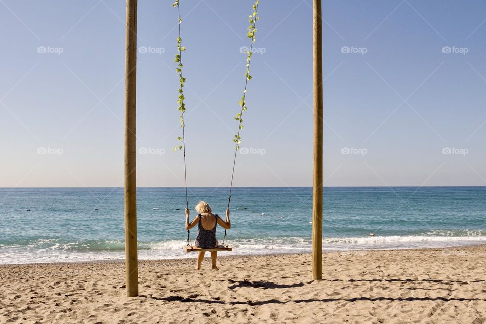 Back view of woman on a rope swing on the beach