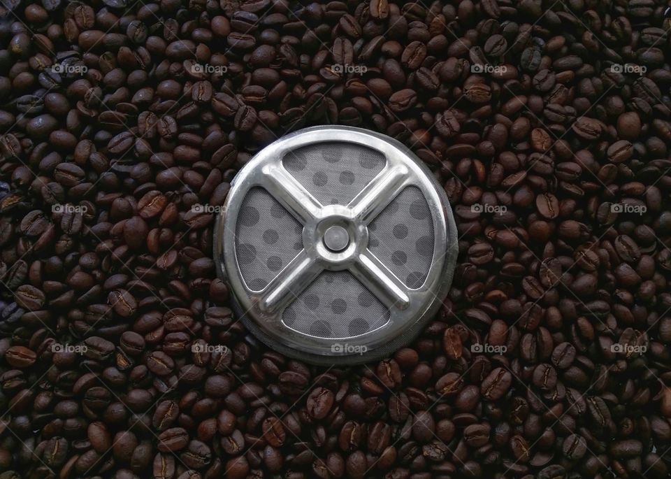 A french press coffee strainer sitting on top of whole coffee beans from above shapes ellipse circles