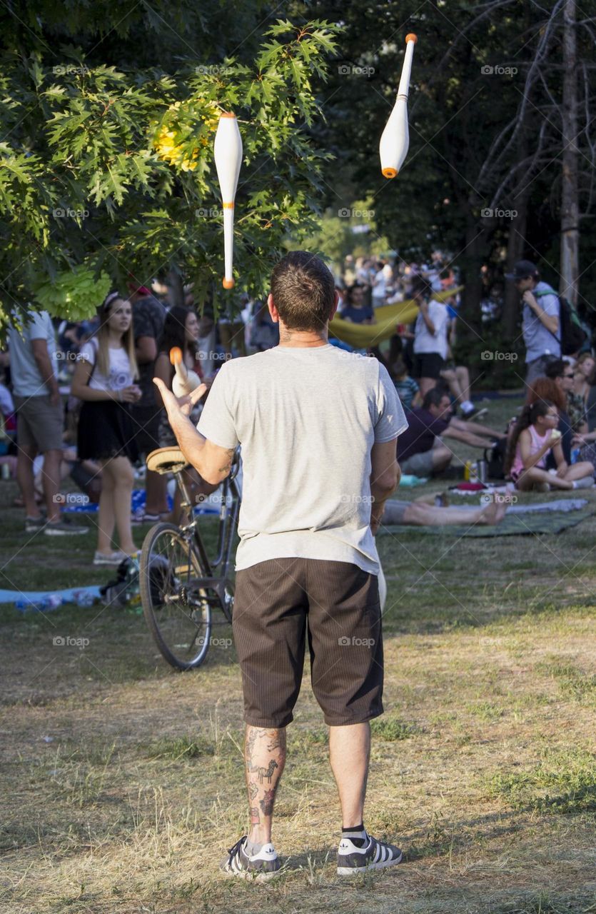 A man juggles clubs in the city park